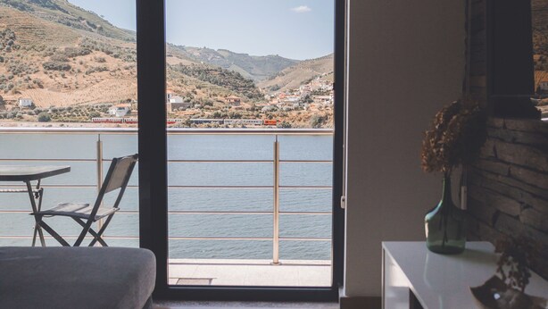 Quarto moderno com uma grande porta de correr de vidro que dá para uma varanda com vista para um corpo de água e colinas.