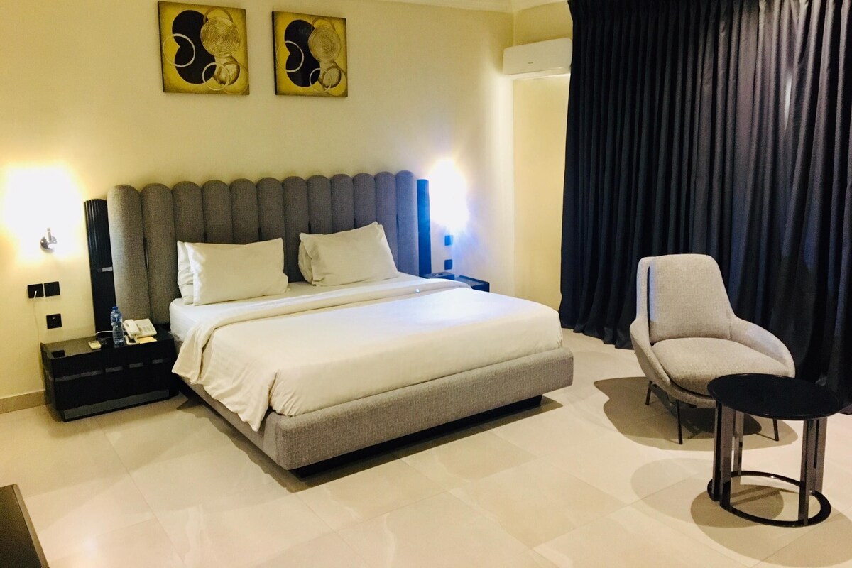 A modern hotel room with a large bed, a chair, and two wall-mounted artworks.
