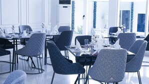 Un'area pranzo moderna con tavoli rotondi, sedie grigie rivestite in tessuto e tavola apparecchiata con stoviglie bianche.