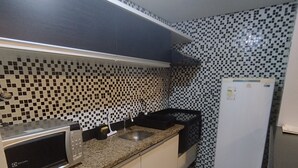 A compact kitchen with a microwave, sink, and a white refrigerator. - Flat Adrianópolis All Suítes - Manaus (Manaus)