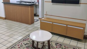 A modern living room with a flat-screen TV, a wooden bench, a small round table, and a kitchen area in the background. - Flat Adrianópolis All Suítes - Manaus (Manaus)