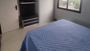 A bedroom with a bed, a wardrobe, a television, and a window with a view of buildings and trees. - Flat Adrianópolis All Suítes - Manaus (Manaus)