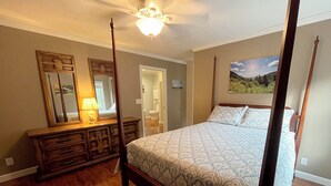 A four-poster bed with a patterned bedspread, a wooden dresser with a mirror, a ceiling fan, and a bathroom visible through an open door. - Meadow Winds, A mountain getaway.  (Galax)