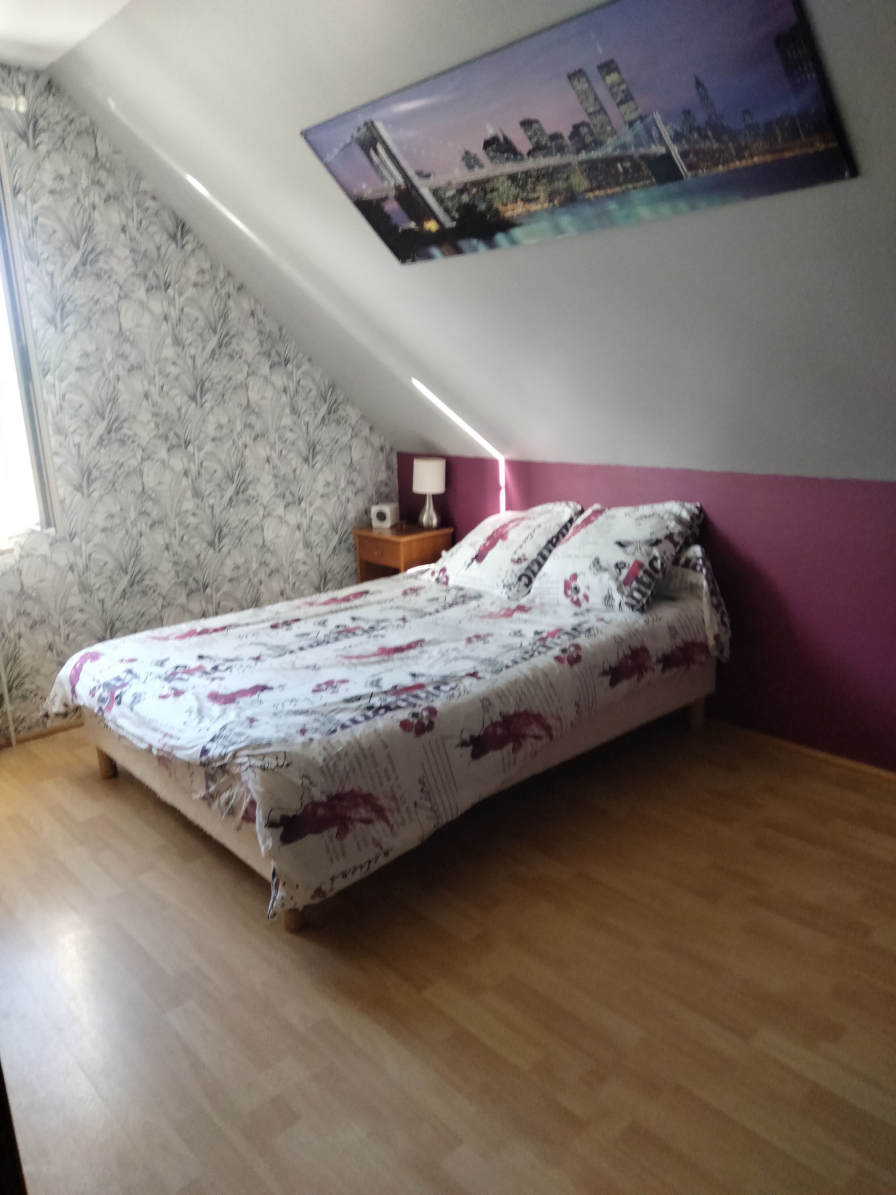 Un dormitorio con una cama, una mesita de noche, una lámpara, un cuadro en la pared y un ventanal.