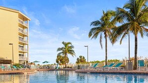 A swimming pool with lounge chairs and palm trees, surrounded by a building with balconies. - 2BR/2BA Beach Condo: Gulf Views & Pools (Treasure Island)