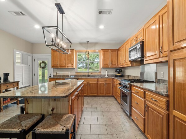 A spacious kitchen with wooden cabinets, a granite countertop, a built-in oven, and a large window offering a view of the outdoors.