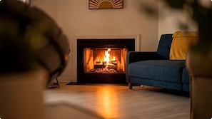 Un salon avec une cheminée, un canapé bleu et un coussin jaune.