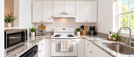 A modern kitchen with white cabinets, a stainless steel stove, a microwave, and a granite countertop.