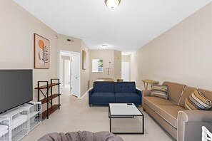 A living room with a sofa, a coffee table, a TV, and a bookshelf. - Suite Life Wilmington-Spacious, Pet-Friendly 1BR, Pool, Balcony, Prime Location (Wilmington)