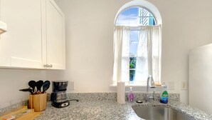 A kitchen with granite countertops, a coffee maker, a sink, and a window with curtains.