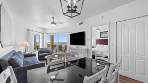 Un salon moderne avec une table à manger en verre, des chaises blanches, un canapé et un ventilateur de plafond.