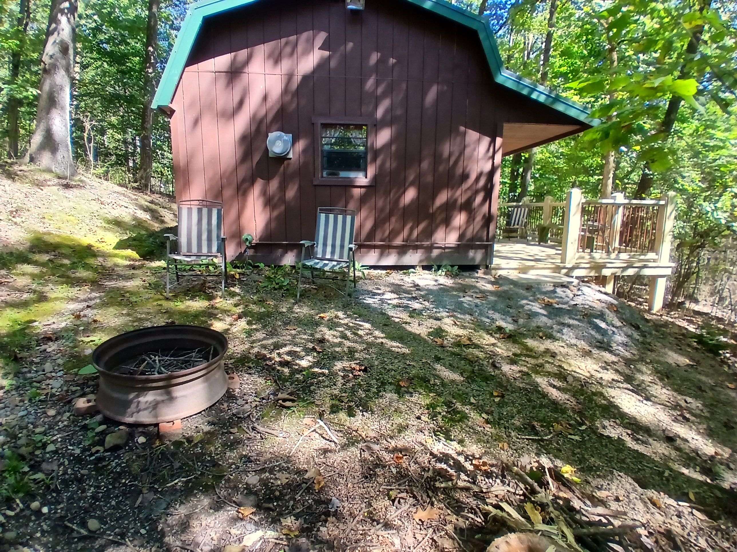 Eine rustikale Holzhütte mit grüner Dachdeckung, einem kleinen Fenster und einer Tür. Vor der Hütte befindet sich eine Feuerstelle.