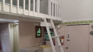 A room with a bunk bed, a small kitchenette, a ladder, a door with a fire alarm, and a ceiling fan. - The Cottage in the Woods, near Deersville and Tappan and Clendening Lakes (Deersville)