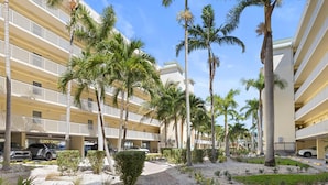 A multi-story hotel with balconies, palm trees, and a parking area. - Spacious 2BR/2BA Condo: Stunning Beach Views (Treasure Island)