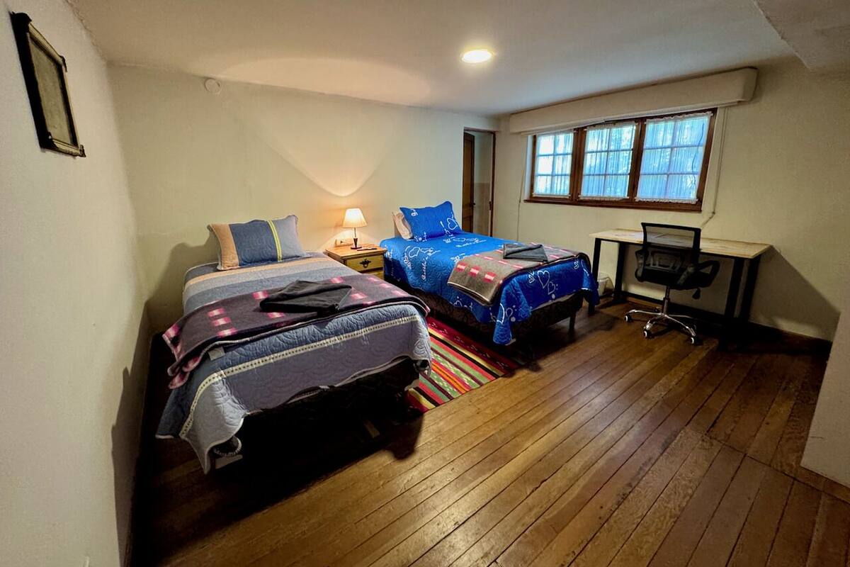 A bedroom with two beds, a desk, and a window.