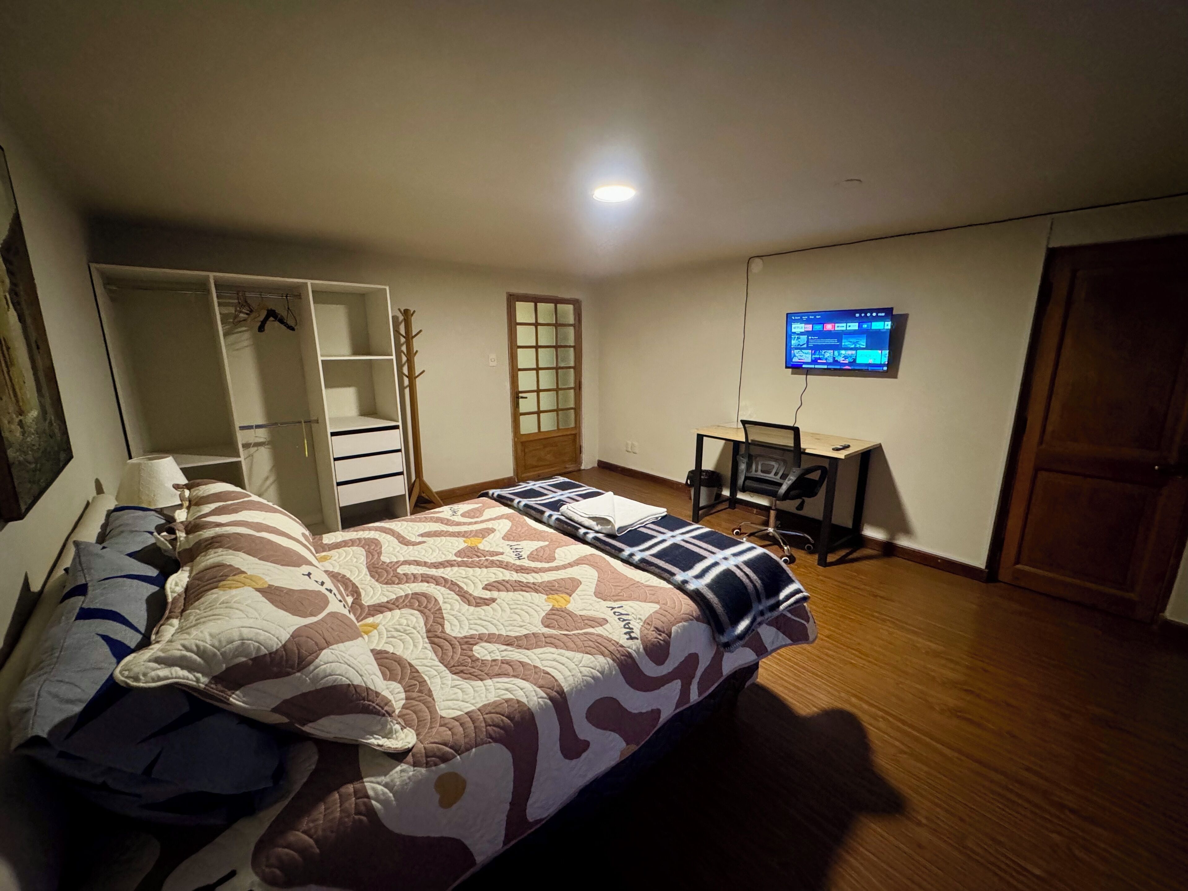 A bedroom with a bed, a desk, a TV, and a wardrobe.