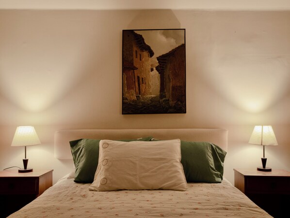 A neatly made bed with a floral-patterned bedspread, two pillows, and two bedside lamps on nightstands.