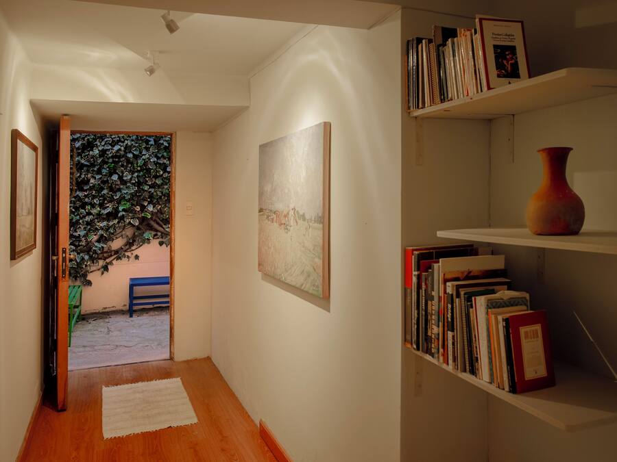 Un couloir avec un plancher en bois, un tapis blanc, une bibliothèque remplie de livres et un vase, ainsi qu’un tableau accroché au mur.