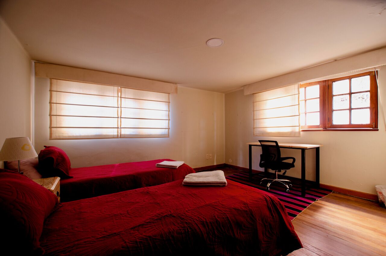 Habitación de hotel con dos camas individuales, un escritorio, una silla y una ventana con persianas.
