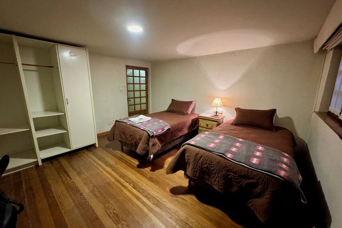 A bedroom with two beds, a wardrobe, a nightstand, and a window with a view.