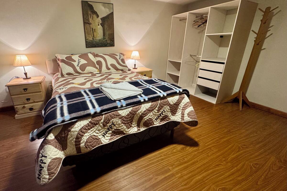 A bedroom with a bed, two bedside tables, a wardrobe, and a painting on the wall.