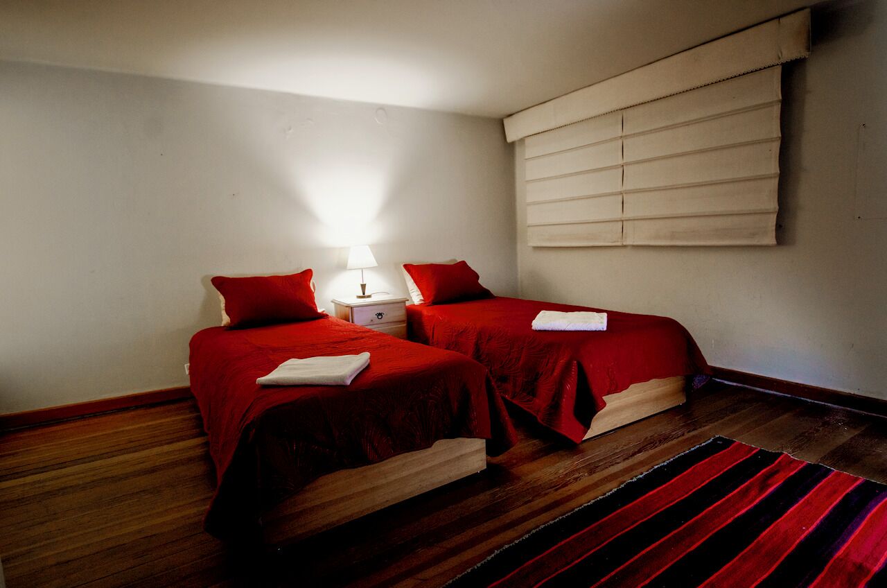 Una habitación con dos camas, cada una con ropa de cama roja y una mesita de noche blanca entre ellas.