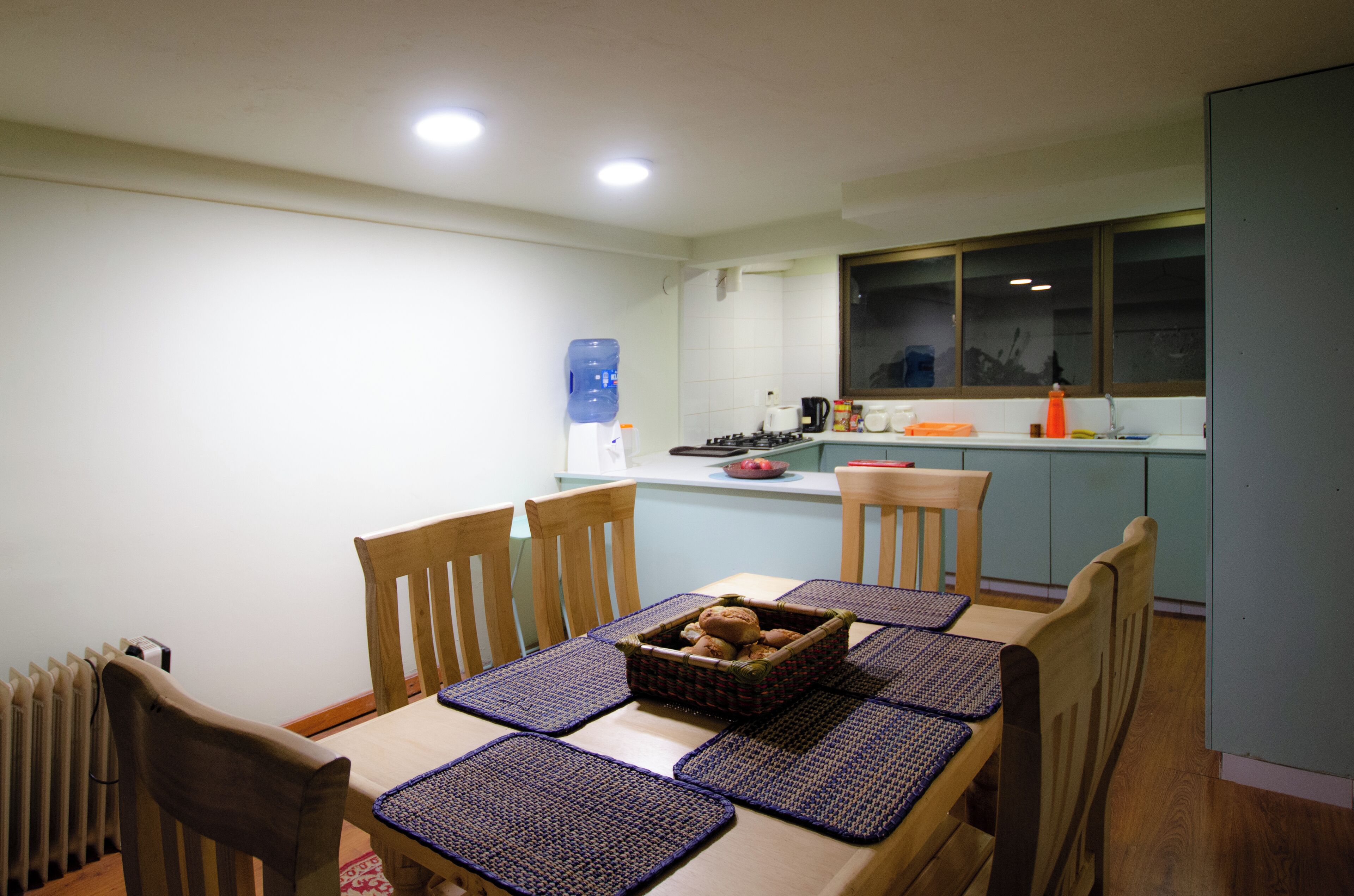 A dining area with a table set for four, wooden chairs, and a water dispenser in the background.