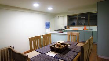 A dining area with a table set for four, wooden chairs, and a water dispenser in the background.