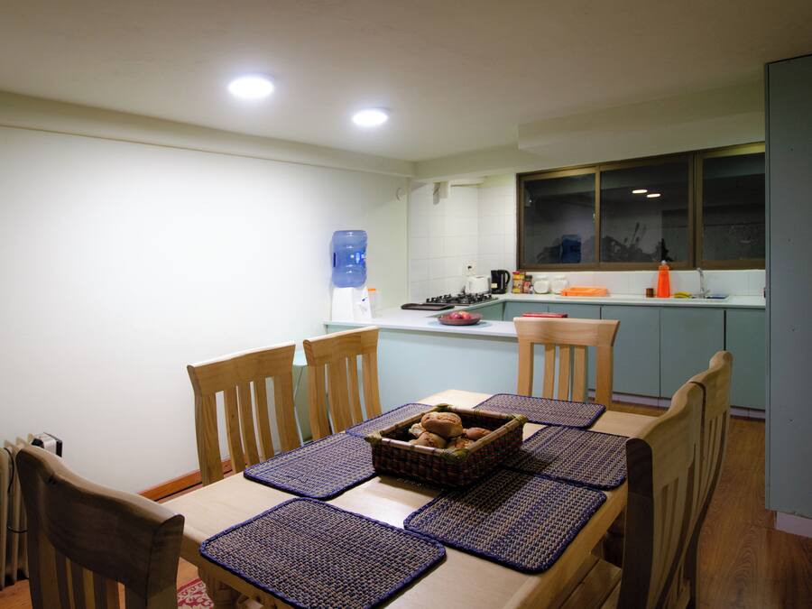 A dining area with a table set for four, wooden chairs, and a water dispenser in the background.