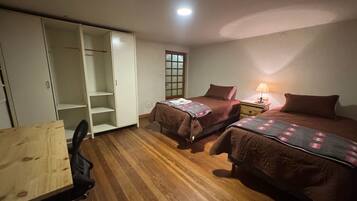 Quarto com duas camas, uma escrivaninha de madeira e um guarda-roupa.