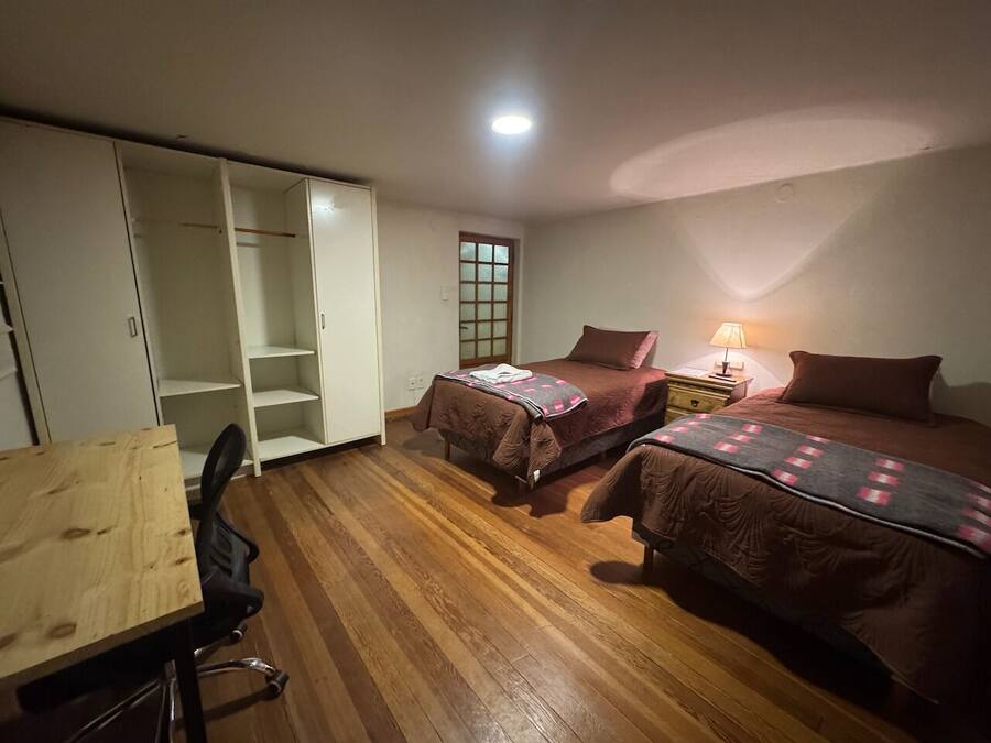 Quarto com duas camas, uma escrivaninha de madeira e um guarda-roupa.