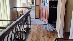 Une terrasse en bois avec une rambarde, une porte donnant accès à une salle de bain et une fenêtre avec des rideaux.