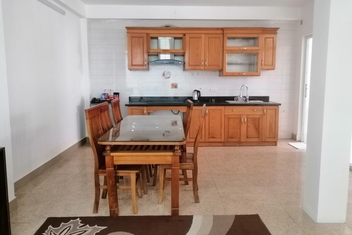 Una cocina compacta con armarios de madera, encimera negra y una mesa de comedor con sillas.