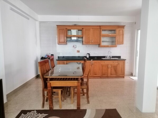 Una cocina compacta con armarios de madera, encimera negra y una mesa de comedor con sillas.