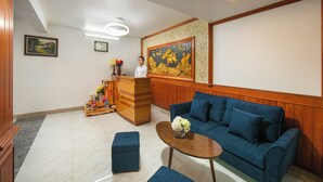 A reception area with a blue sofa, a wooden reception desk, and a painting on the wall. - Mia Sen Vong Hotel Hanoi (Hanoi)