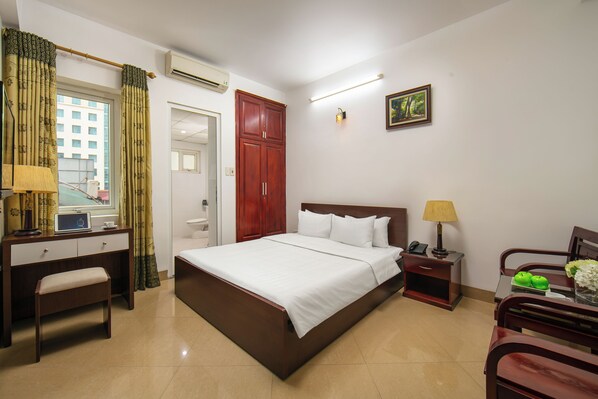 Habitación de hotel con cama, escritorio, silla, mesita de noche, lámpara y un cuadro en la pared.