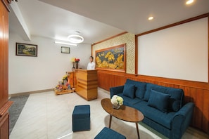A reception area with a blue sofa, a wooden reception desk, and a painting on the wall. - Mia Sen Vong Hotel Hanoi (Hanoi)