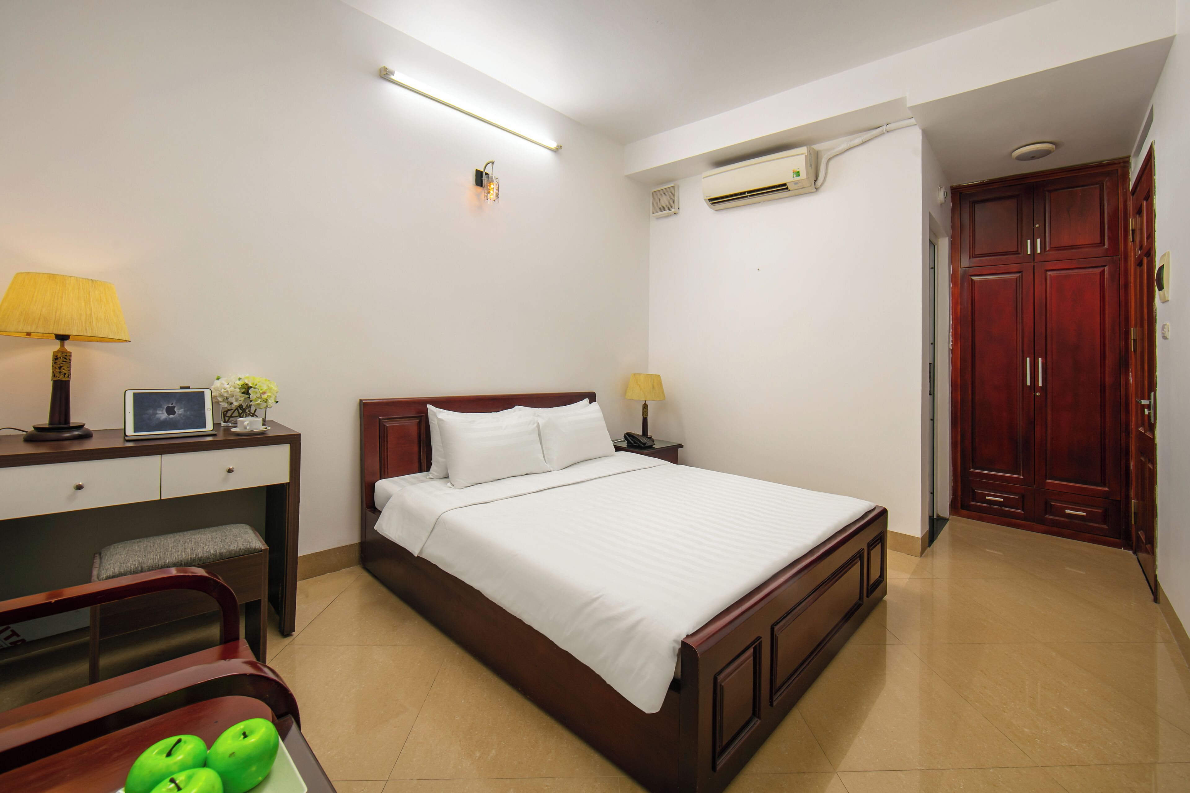 Habitación de hotel ordenada con cama, mesita de noche, lámpara y escritorio con silla.