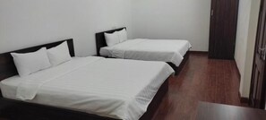 Una habitación con dos camas individuales, cada una con cabecero de madera y ropa de cama blanca. El suelo es de baldosas y la puerta es de madera.