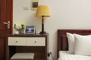 Habitación de hotel con escritorio de madera, lámpara, cuadro enmarco, pequeño jarrón con flores y cama con almohadas blancas.