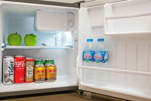 Un refrigerador con dos manzanas verdes, dos botellas de una bebida azul y varias latas de bebidas.