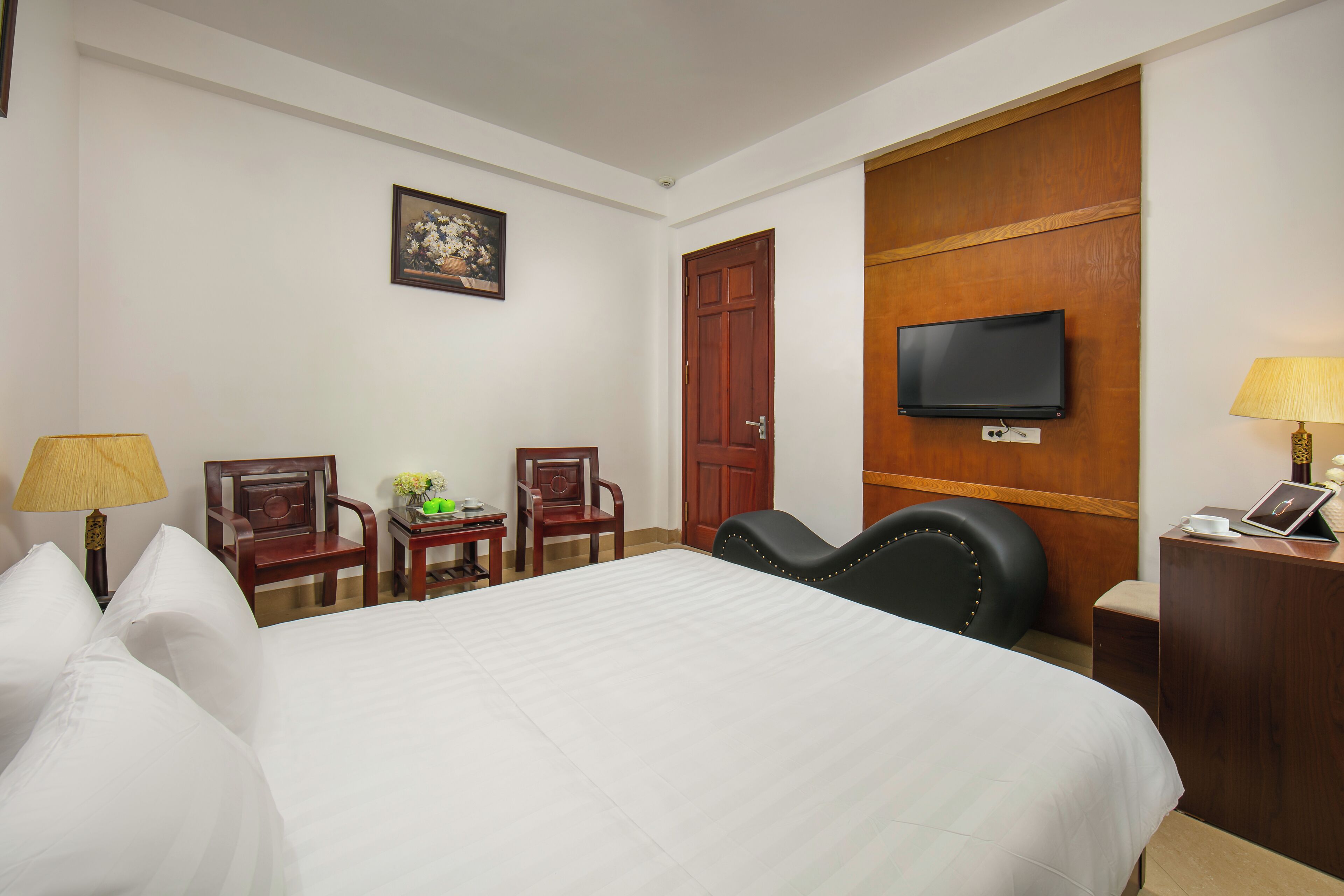 Habitación de hotel con una cama grande, dos sillas, un escritorio con una computadora portátil, un televisor y una puerta.