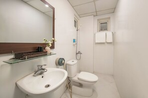 Un baño con lavamanos, inodoro y ducha blancos. Hay un espejo sobre el lavamanos y una ventana pequeña sobre el inodoro.