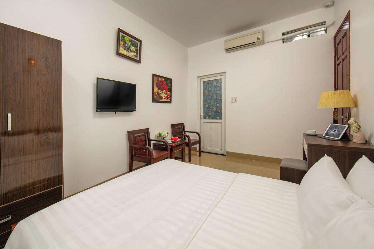 Habitación de hotel con una cama grande, televisión, escritorio con sillas, puerta y ventana.