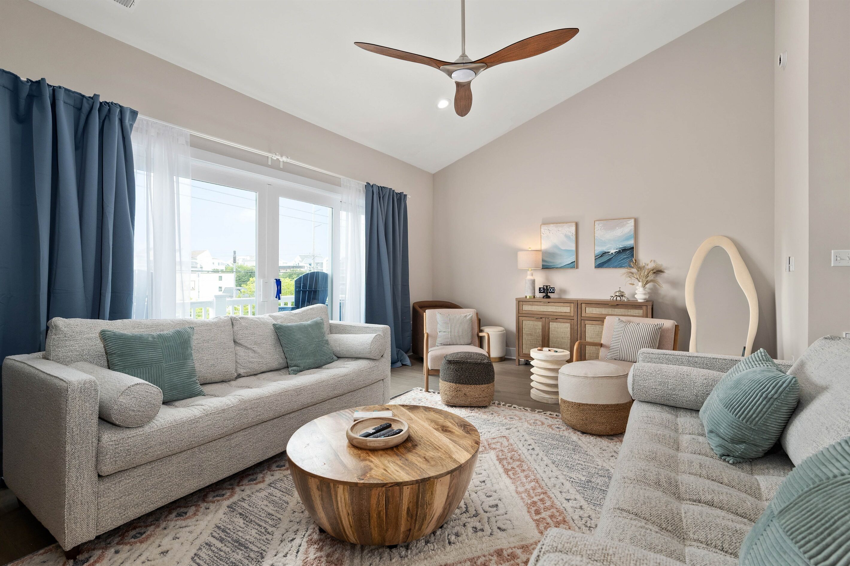 A modern living room with a sofa, ottoman, and coffee table, a ceiling fan, and a view of the outdoors.