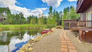 Una cabaña junto al lago con un camino de grava que lleva a un muelle, un kayak y una terraza de madera con mobiliario exterior.