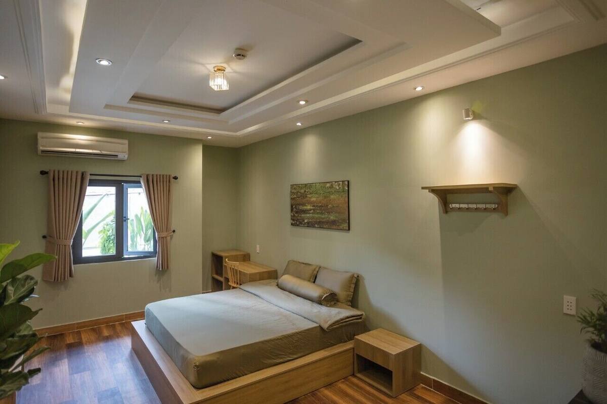 A bedroom with a bed, bedside tables, a nightstand, an air conditioning unit, a window with curtains, and a wall-mounted shelf.