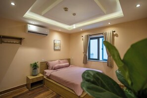 Un dormitorio con cama, mesita de noche, aire acondicionado, ventana con cortinas e iluminación en el techo.