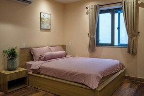 Une chambre à coucher comprenant un lit, une table de chevet, une plante en pot, une fenêtre avec des rideaux et un interrupteur fixé au mur.