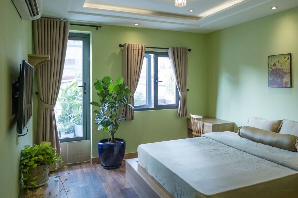 A bedroom with a bed, a potted plant, a desk, and a window with curtains.